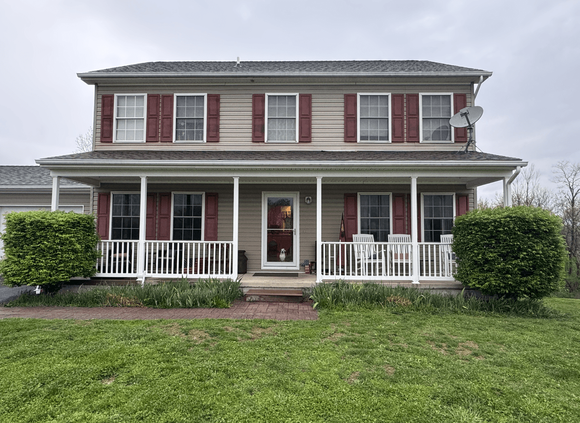 A house with a front porch, featuring green grass and shrubs, awaiting landscaping updates.