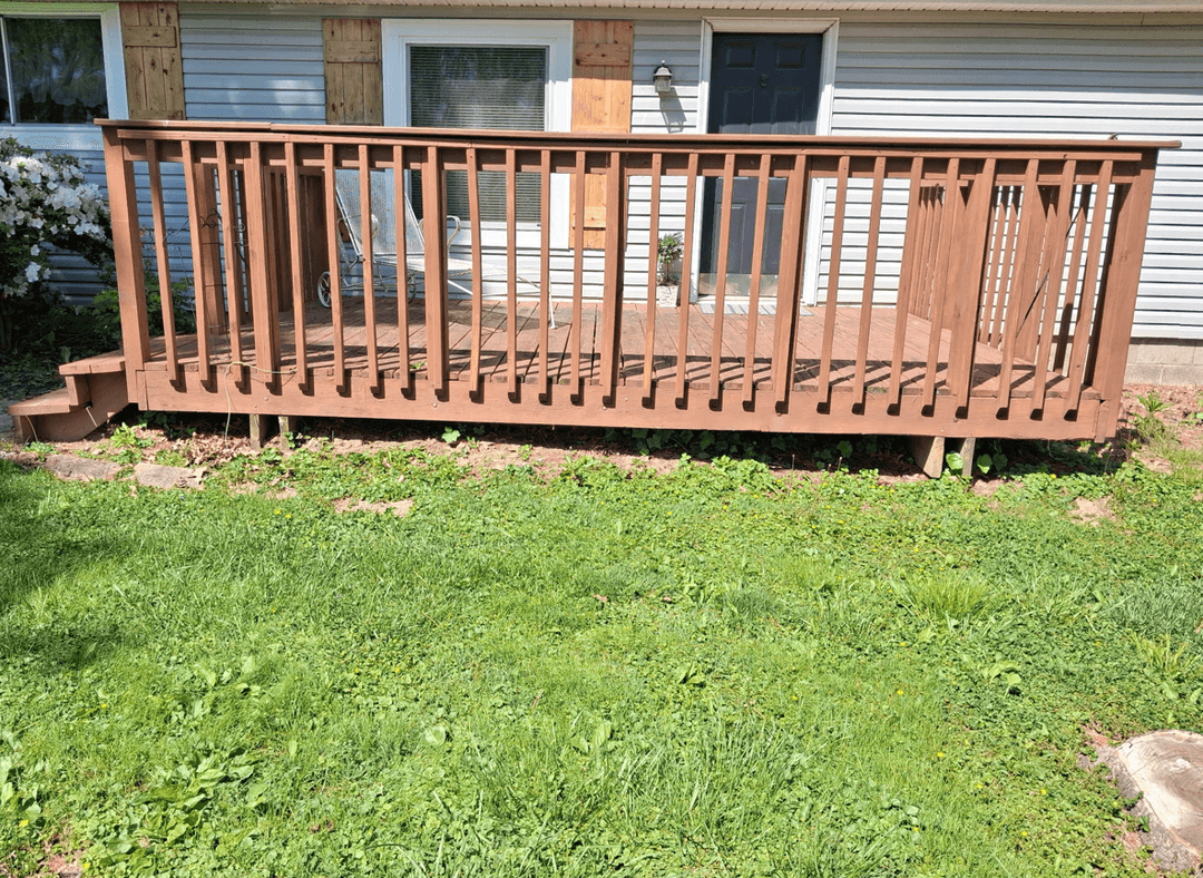 A wooden deck with a railing in a grassy yard, showing the layout for removal.