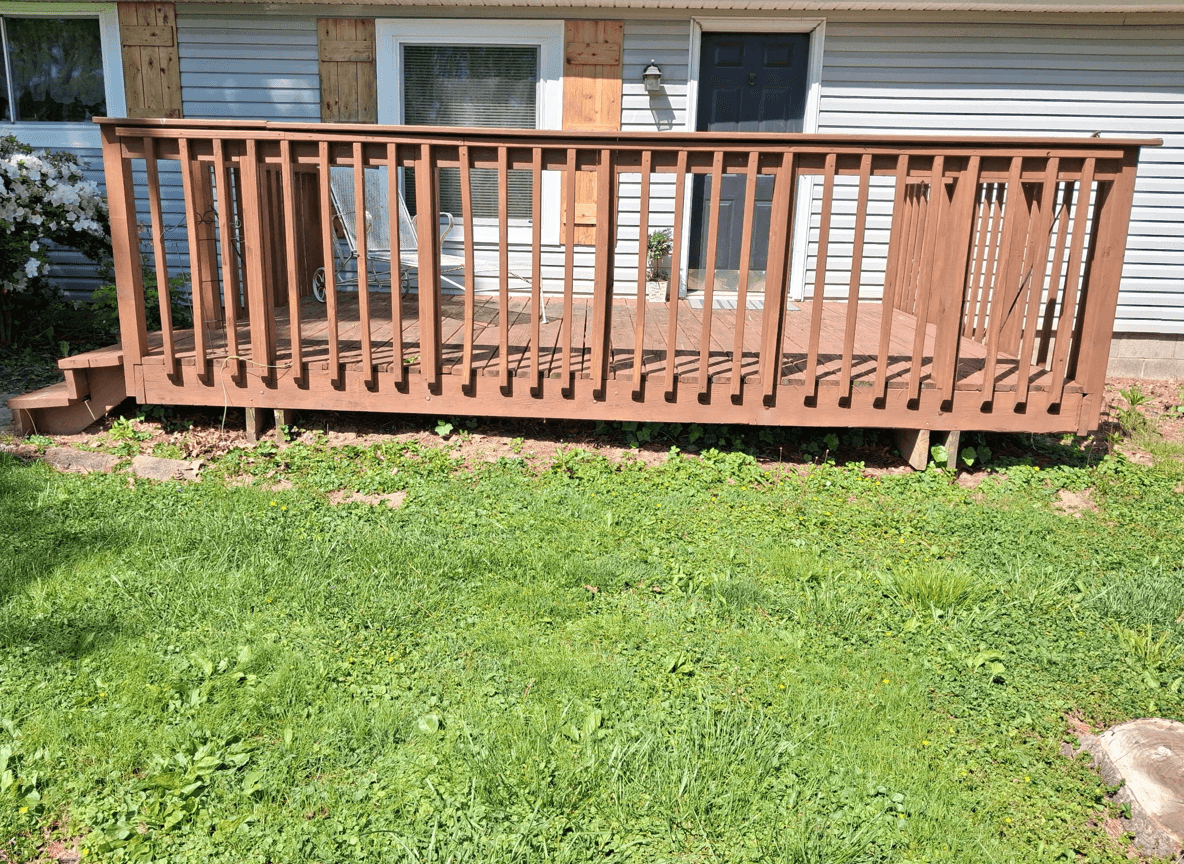 A wooden deck with a railing in a grassy yard, showing the layout for removal.