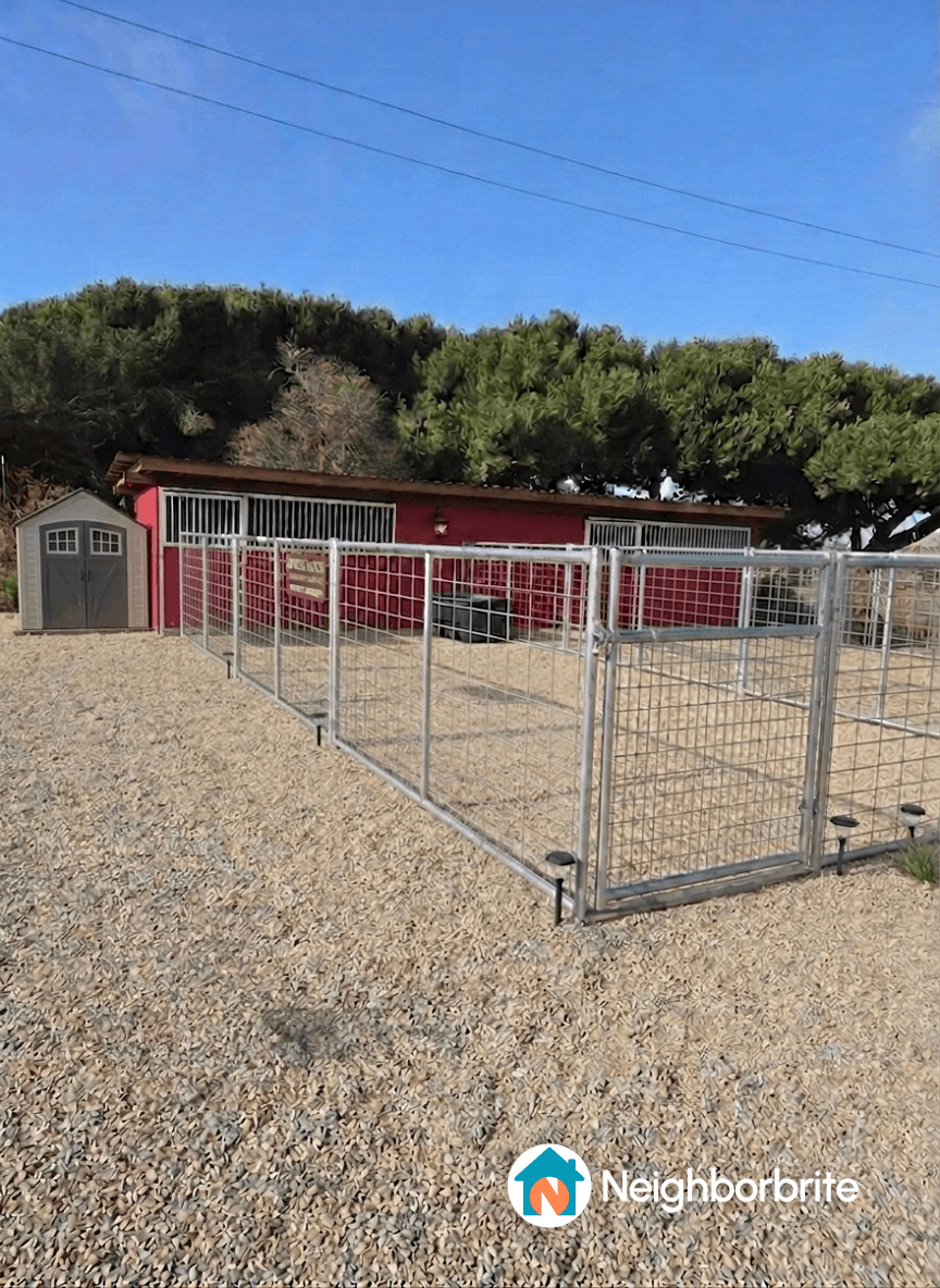 A view of a stable with fencing and a storage shed.