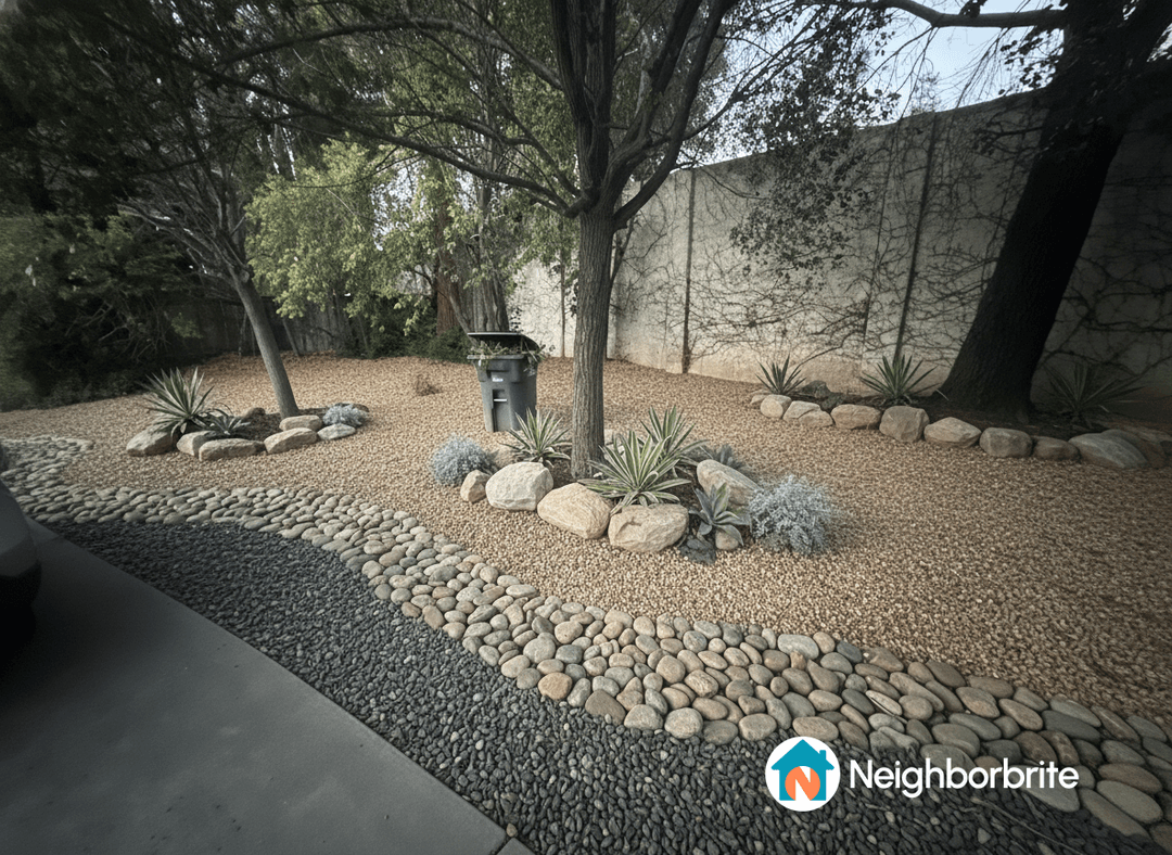 A landscaped yard with rocks, plants, and a trash bin.