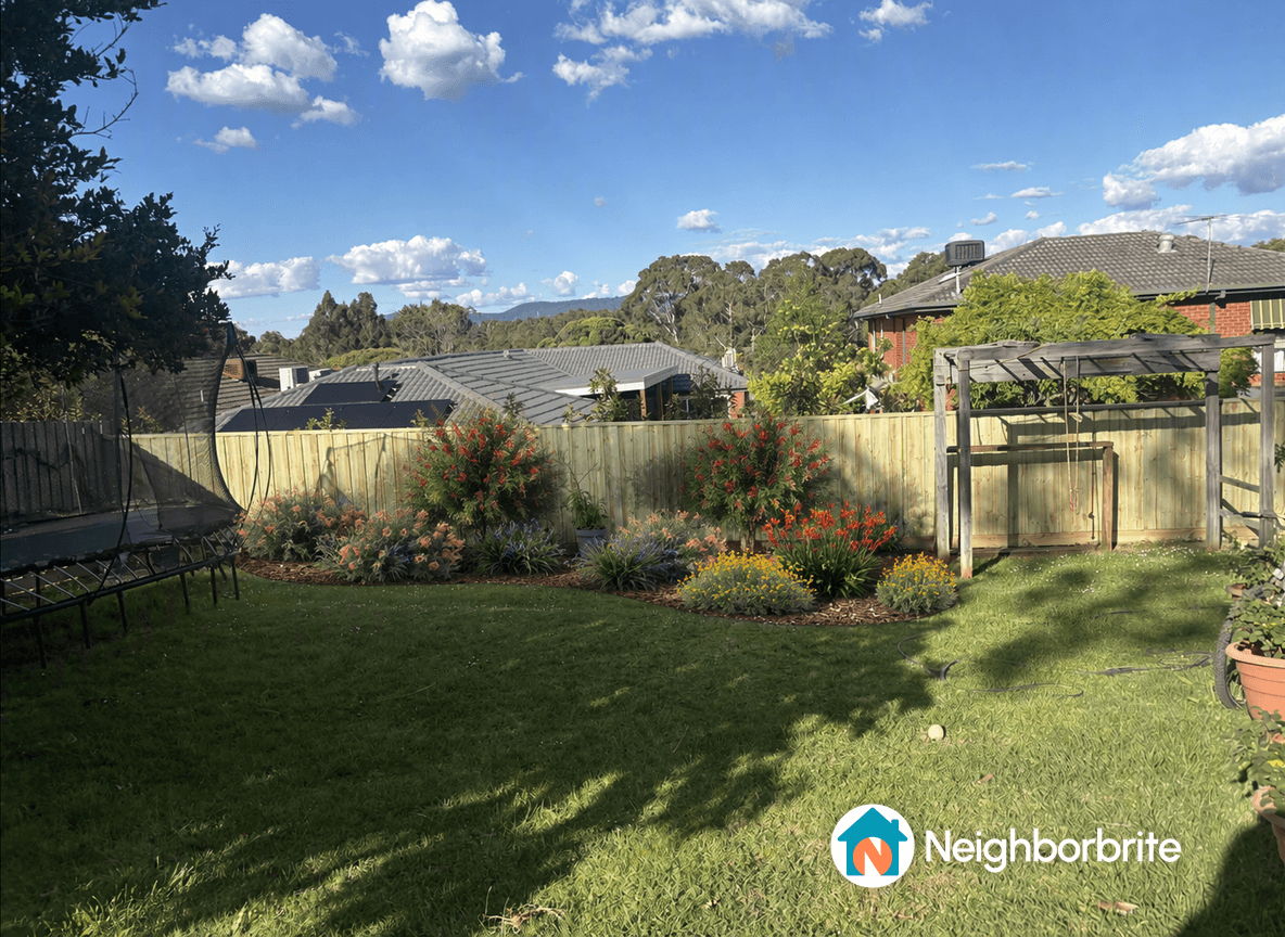 A backyard with flowers, grass, and a wooden fence under a blue sky.
