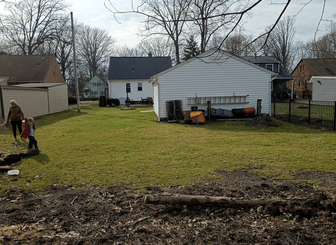 A backyard with a child playing and an adult nearby, showcasing a grassy area and surrounding homes.