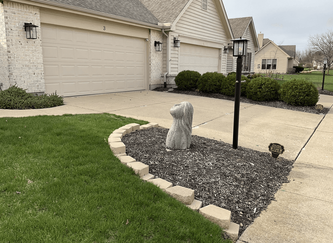 A landscaped area with a stone feature, neat grass, and shrubs.