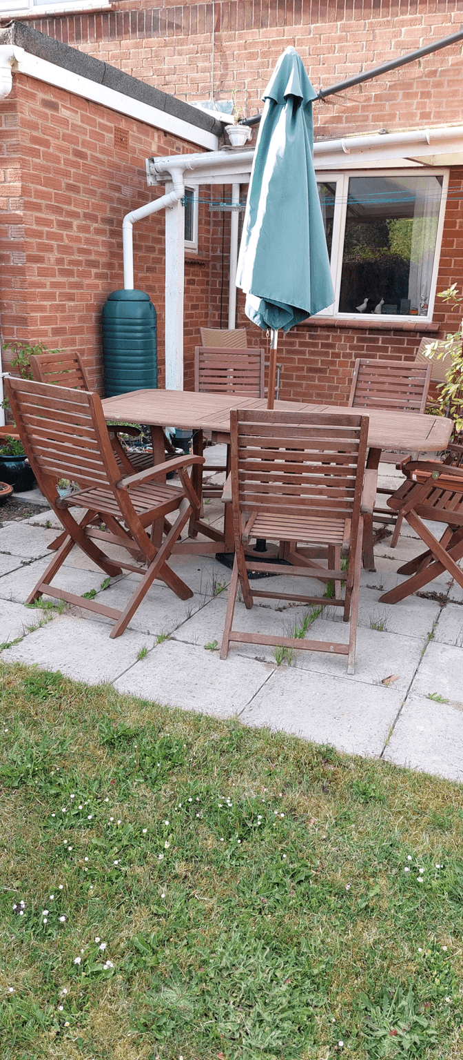A wooden patio set with chairs and an umbrella in a garden area.