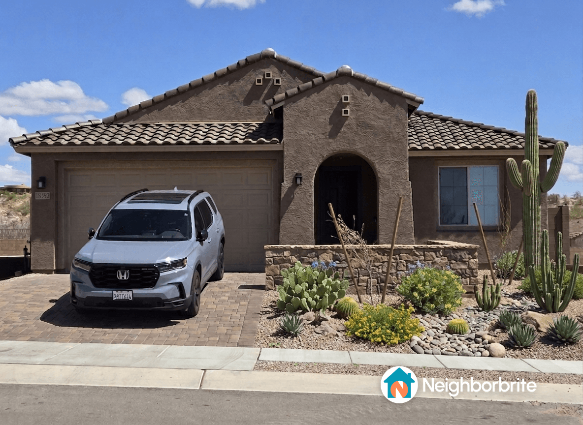 A house with a rock wall and desert landscaping, featuring a car parked in the driveway.