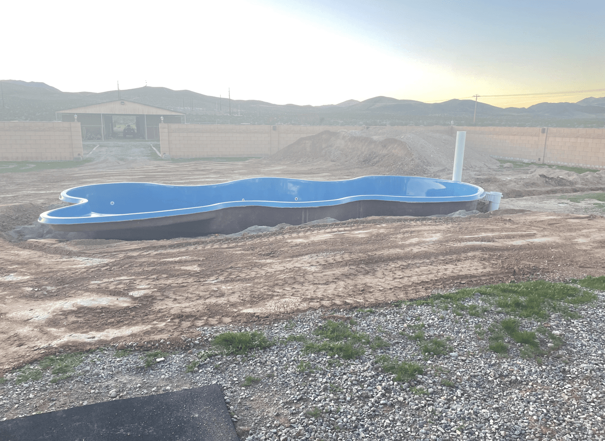 A blue pool surrounded by dirt and gravel, with mountains in the background.