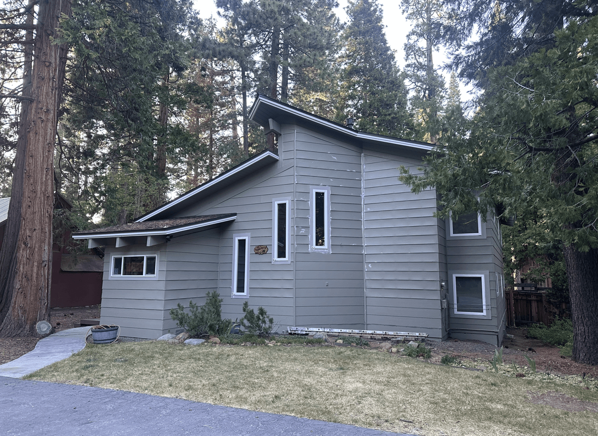 A house surrounded by trees, seeking large rocks and evergreen bushes.