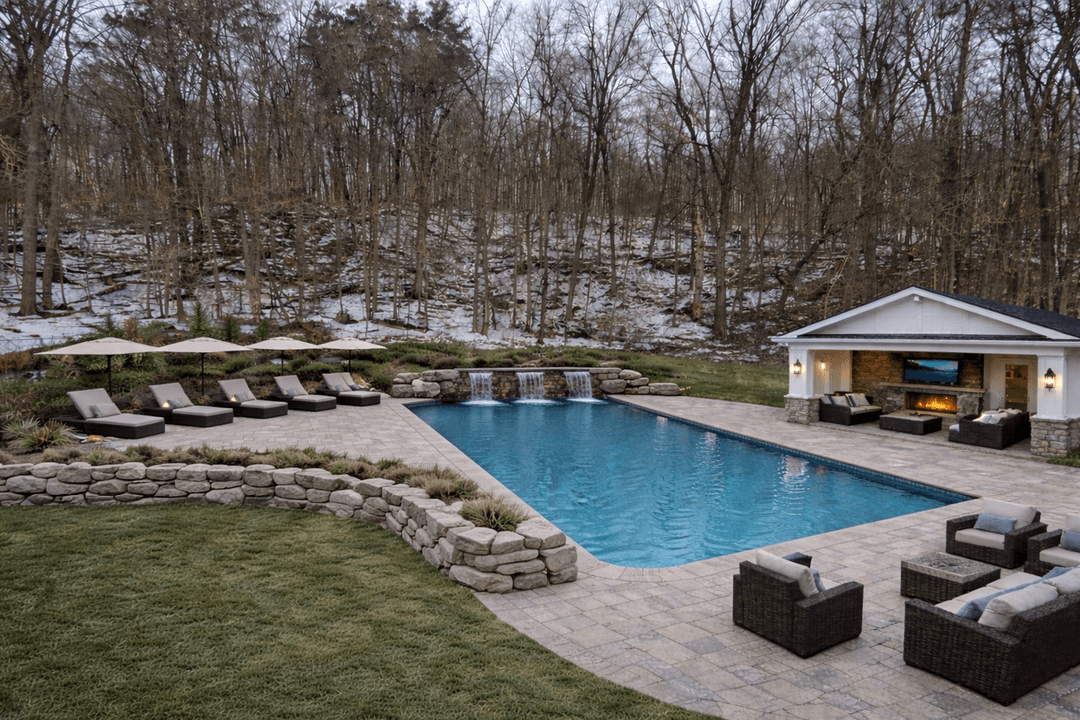 A backyard pool with lounge chairs and a stone wall, surrounded by trees.