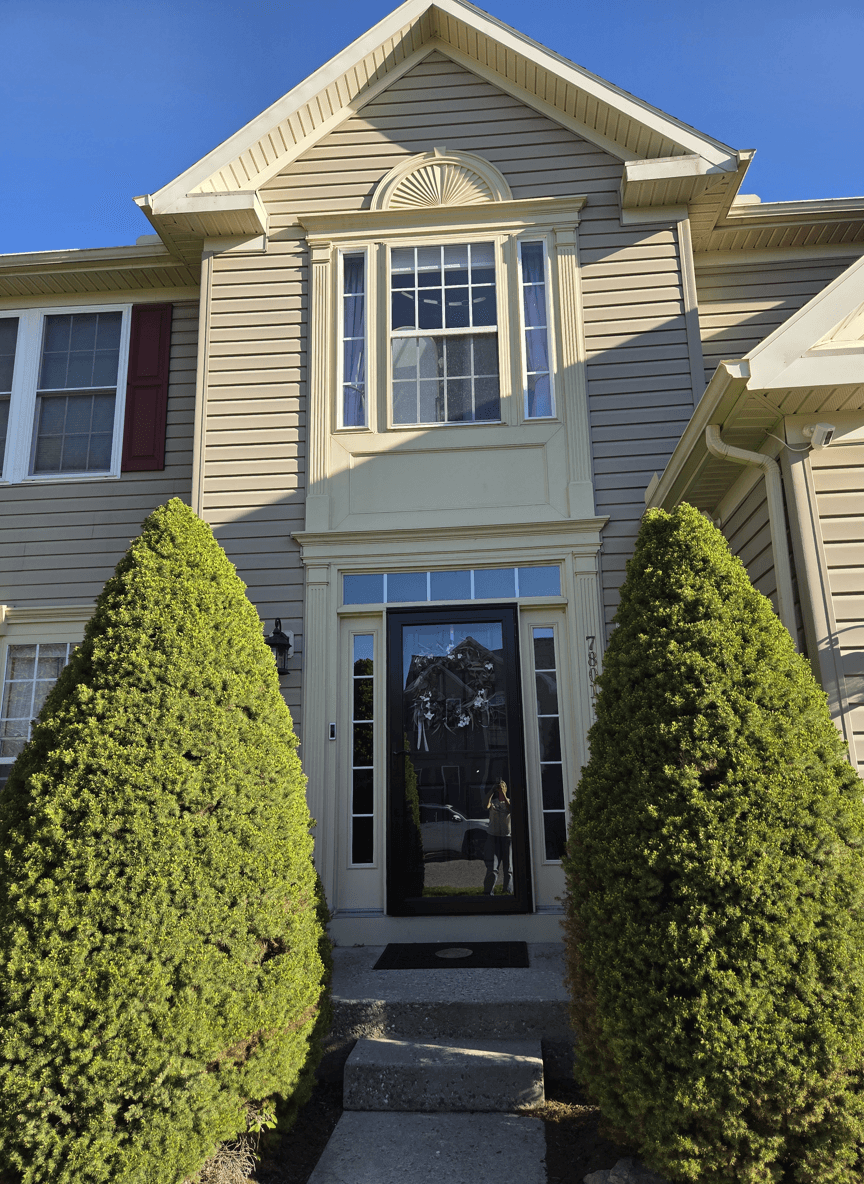 Front porch of a house with two large shrubs and a black door.