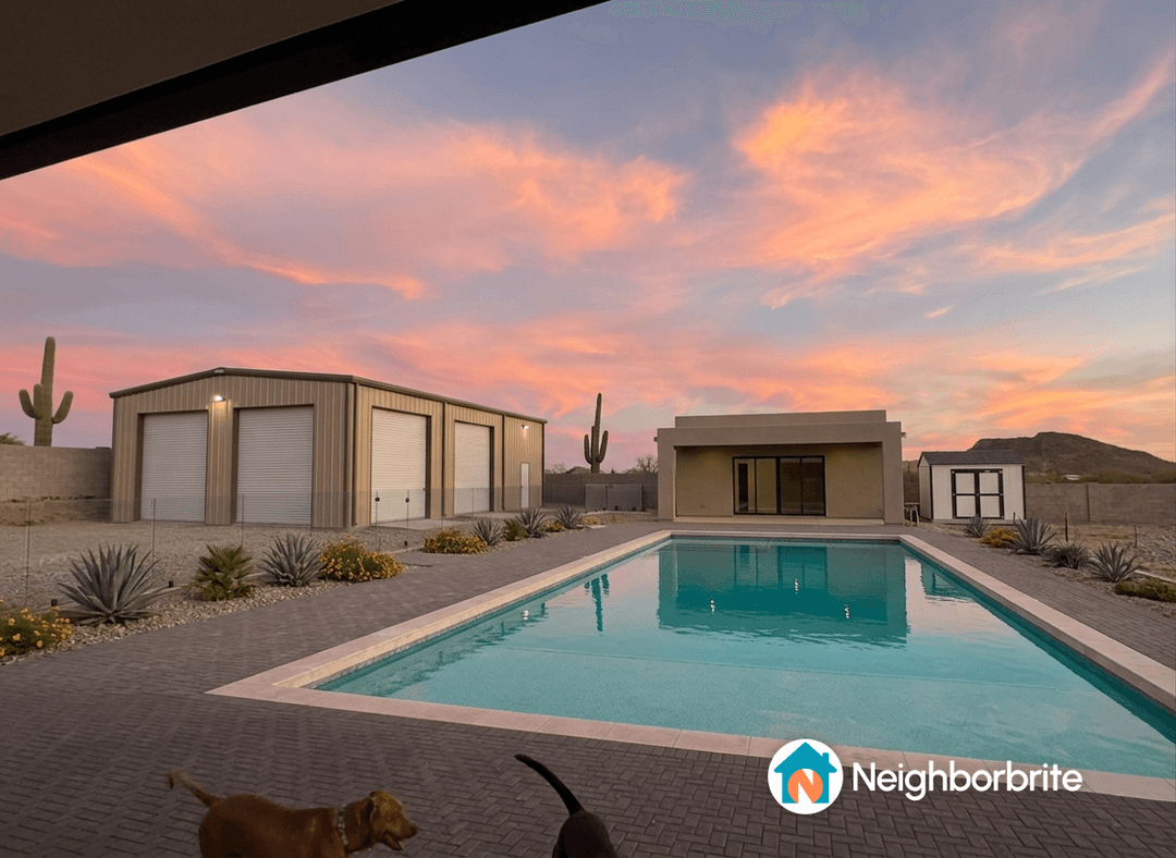 View of a backyard with a pool, garage, and retaining wall at sunset.