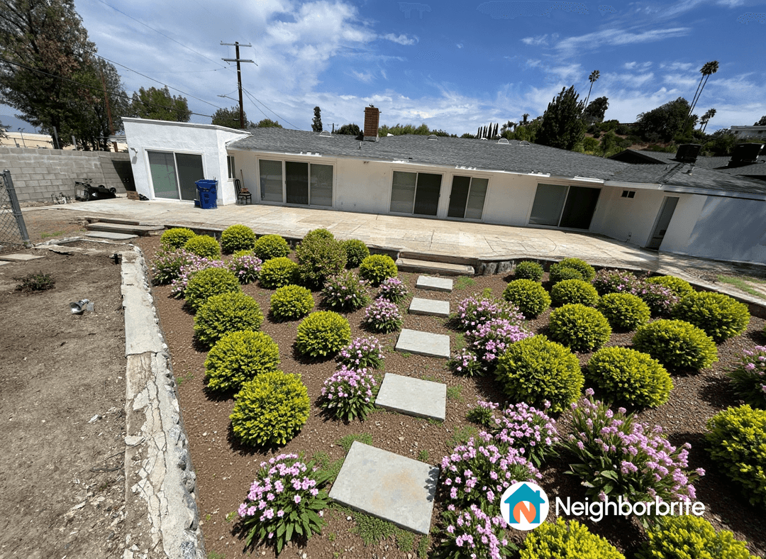 A landscaped yard featuring bushes, flowers, and stone pathways.